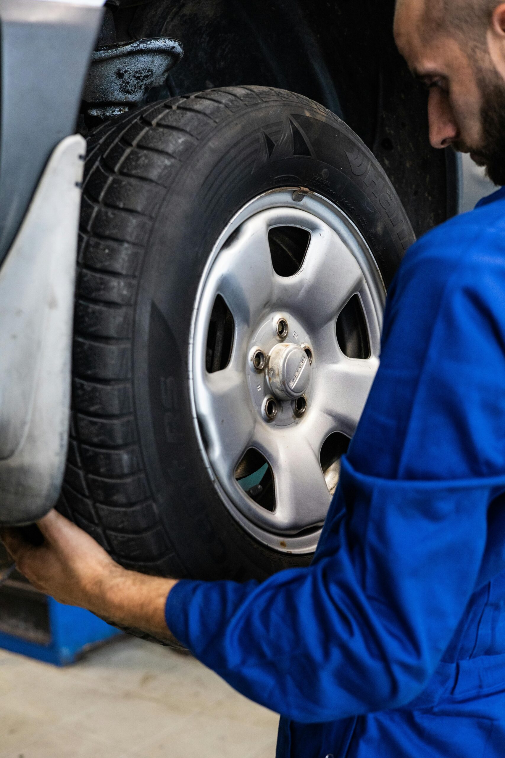 A mechanic in blue uniform closely examines a car wheel for repairs.